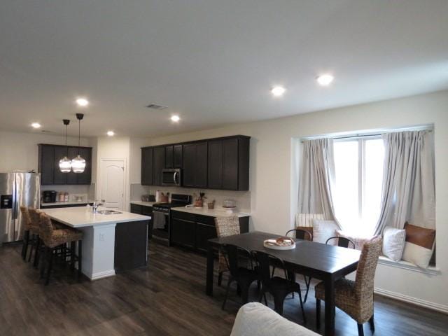 kitchen with dark hardwood / wood-style flooring, hanging light fixtures, appliances with stainless steel finishes, and an island with sink