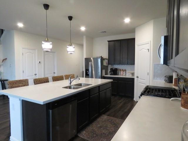 kitchen with sink, hanging light fixtures, decorative backsplash, a center island with sink, and appliances with stainless steel finishes