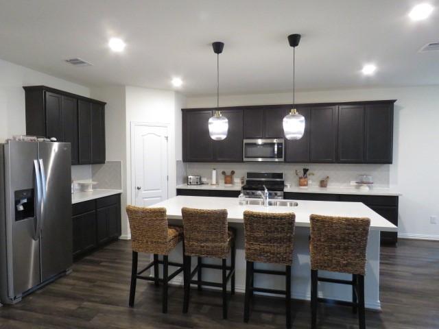 kitchen featuring a kitchen island with sink, hanging light fixtures, dark hardwood / wood-style floors, and appliances with stainless steel finishes