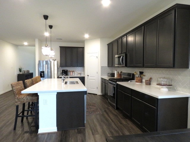 kitchen featuring dark hardwood / wood-style floors, decorative backsplash, stainless steel appliances, and a kitchen island with sink