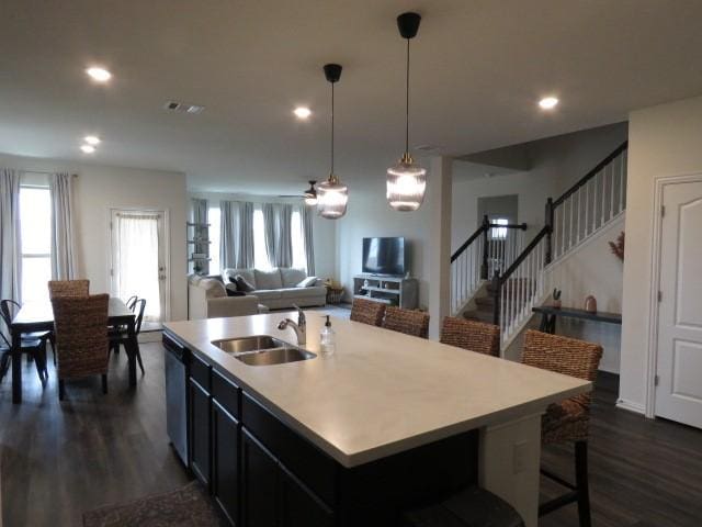 kitchen with sink, dark hardwood / wood-style flooring, stainless steel dishwasher, an island with sink, and pendant lighting