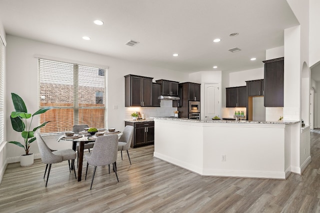 kitchen featuring light stone countertops, appliances with stainless steel finishes, light hardwood / wood-style flooring, and backsplash