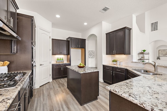 kitchen with a textured ceiling, light stone countertops, light hardwood / wood-style flooring, sink, and a center island