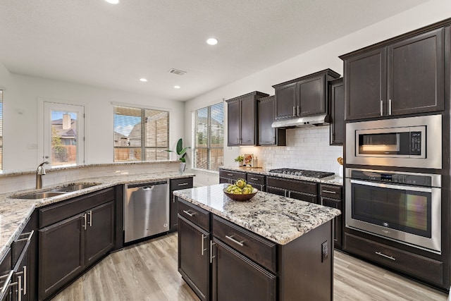 kitchen with sink, light wood-type flooring, stainless steel appliances, dark brown cabinetry, and decorative backsplash