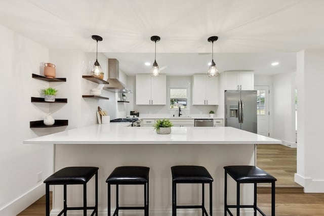 kitchen with appliances with stainless steel finishes, wall chimney exhaust hood, white cabinetry, and kitchen peninsula