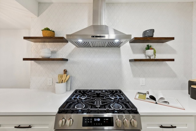 kitchen featuring wall chimney exhaust hood, white cabinetry, tasteful backsplash, and stainless steel gas range oven