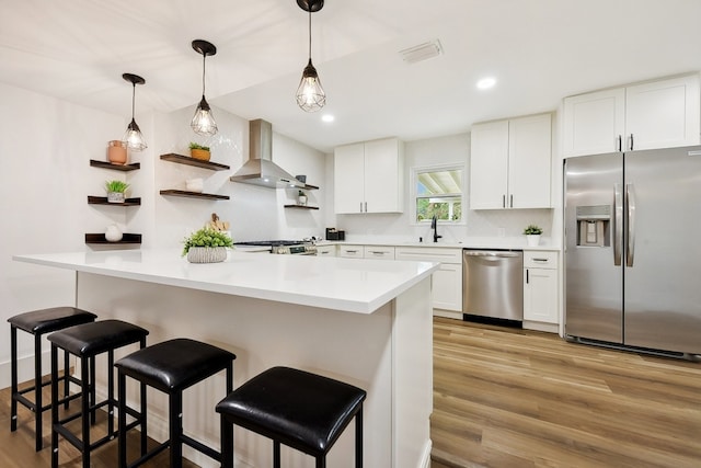 kitchen with wall chimney exhaust hood, appliances with stainless steel finishes, light wood-type flooring, and white cabinets