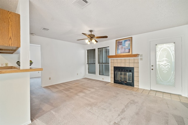 unfurnished living room with ceiling fan, a fireplace, a textured ceiling, and light colored carpet