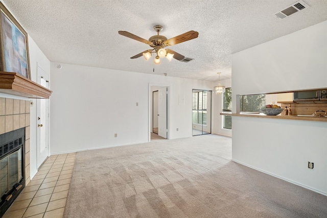 unfurnished living room with a textured ceiling, a tiled fireplace, light colored carpet, and ceiling fan