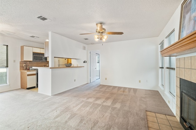 unfurnished living room with light carpet, a textured ceiling, a fireplace, and ceiling fan