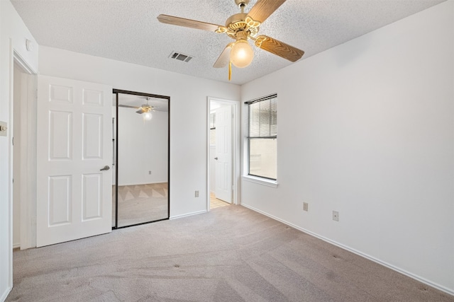 unfurnished bedroom featuring light carpet, a textured ceiling, a closet, and ceiling fan