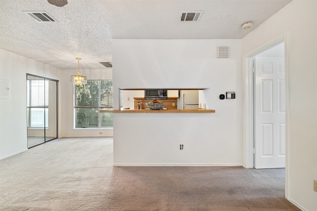 kitchen with light colored carpet, a textured ceiling, white fridge, and decorative light fixtures