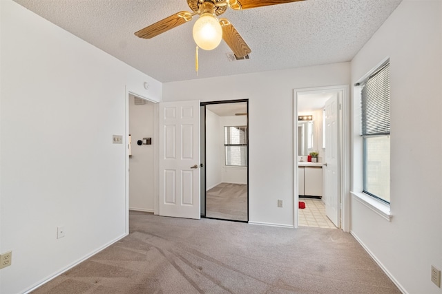 unfurnished bedroom featuring multiple windows, a textured ceiling, light colored carpet, and ceiling fan