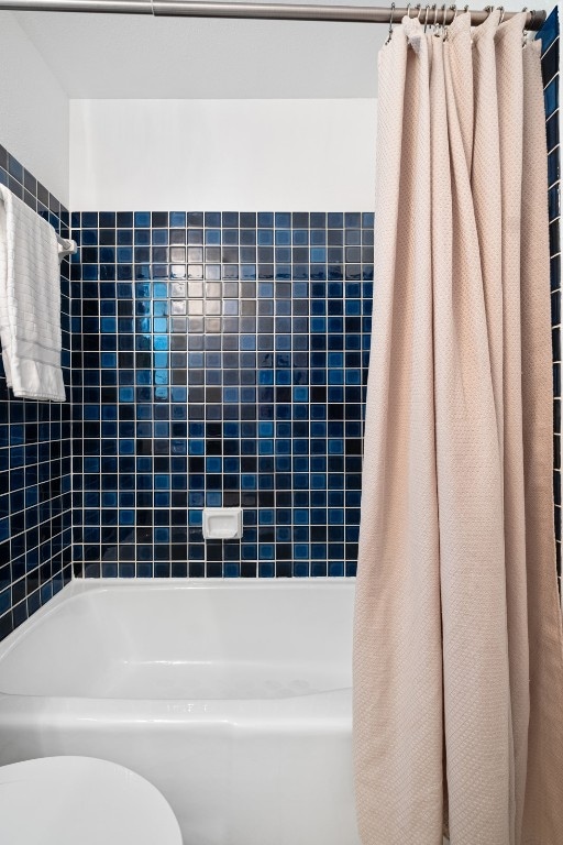 bathroom featuring toilet and shower / bathtub combination with curtain