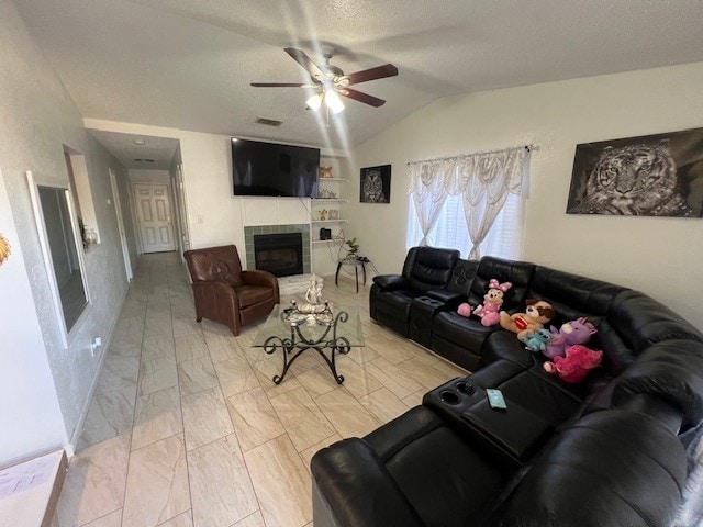 living room featuring a textured ceiling, ceiling fan, a fireplace, and vaulted ceiling