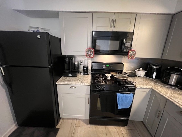 kitchen with gray cabinets, decorative backsplash, light stone countertops, and black appliances