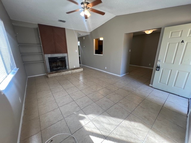 unfurnished living room featuring ceiling fan, a textured ceiling, vaulted ceiling, and light tile patterned floors