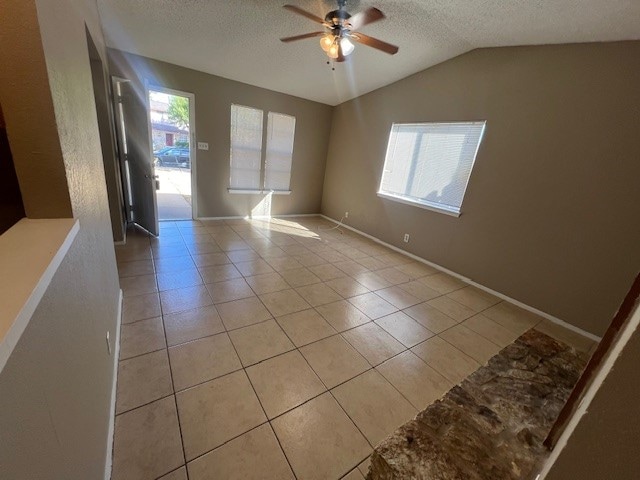 empty room featuring a textured ceiling, ceiling fan, light tile patterned flooring, and vaulted ceiling