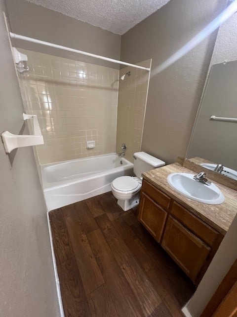 full bathroom with a textured ceiling, hardwood / wood-style floors, toilet, tiled shower / bath, and vanity