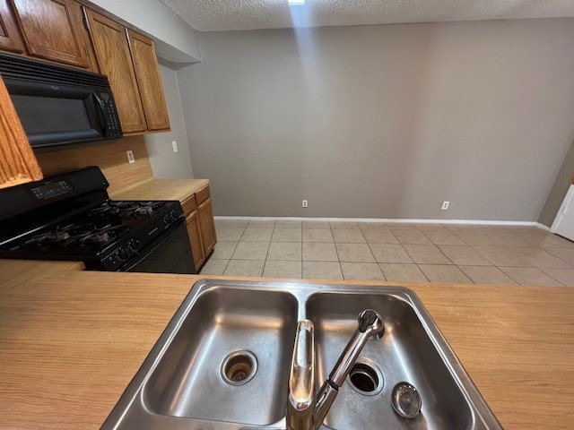 kitchen with sink, a textured ceiling, black appliances, and light tile patterned flooring