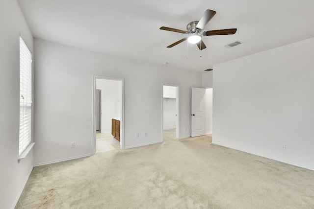 unfurnished bedroom featuring a walk in closet, ensuite bath, a closet, ceiling fan, and light colored carpet