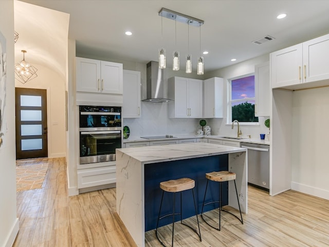 kitchen featuring wall chimney range hood, a center island, white cabinets, light wood-type flooring, and appliances with stainless steel finishes