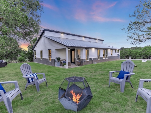 back house at dusk with a lawn, a patio, and a fire pit