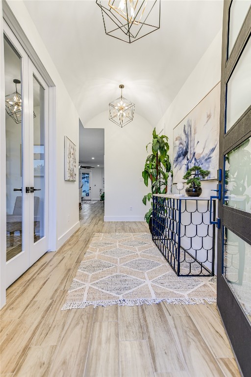 hall with french doors, a notable chandelier, wood-type flooring, and lofted ceiling