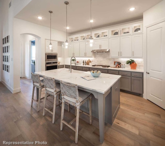 kitchen with hanging light fixtures, appliances with stainless steel finishes, wood-type flooring, and a kitchen island with sink