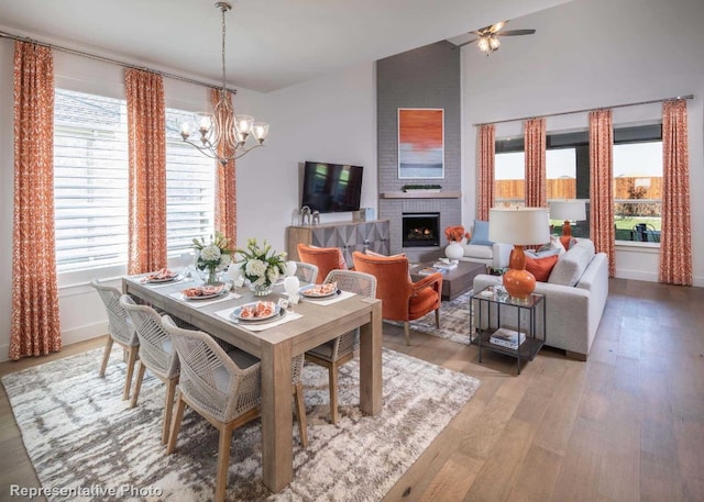 dining area with vaulted ceiling, a brick fireplace, ceiling fan with notable chandelier, and light wood-type flooring