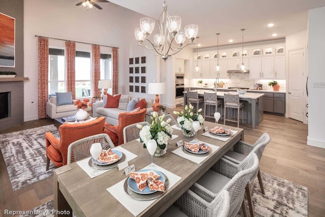 dining room with lofted ceiling, light wood-type flooring, a fireplace, ceiling fan with notable chandelier, and sink