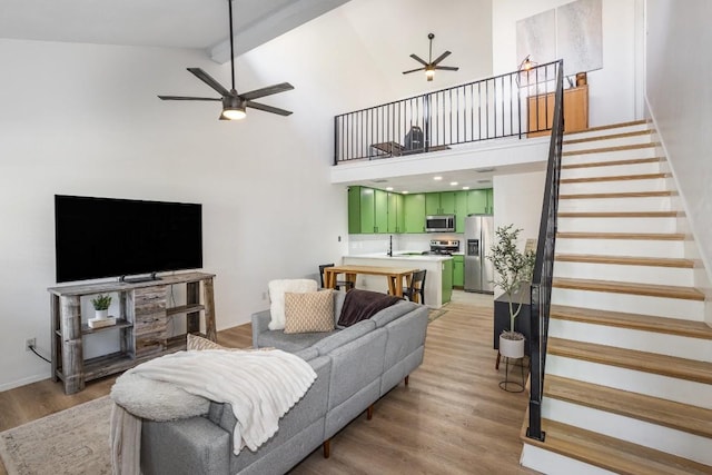 living room with beamed ceiling, high vaulted ceiling, ceiling fan, and light wood-type flooring