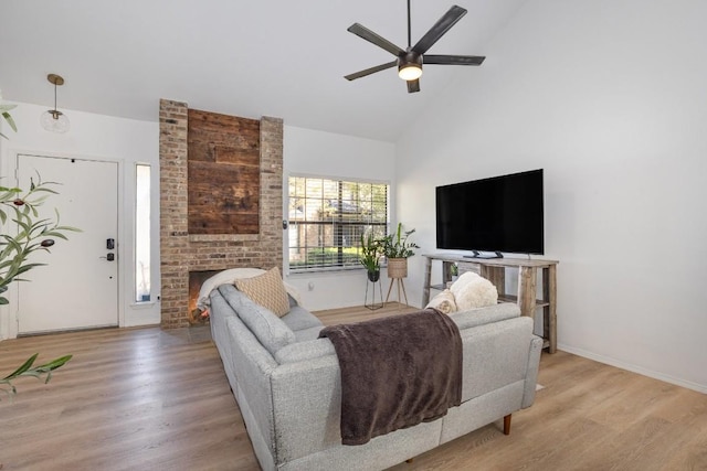 living room featuring ceiling fan, high vaulted ceiling, a fireplace, and light hardwood / wood-style floors