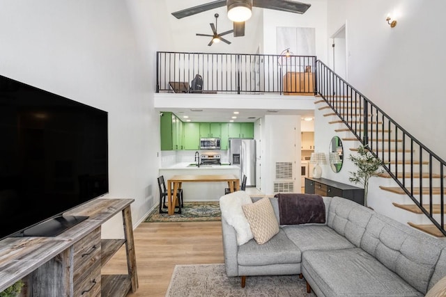 living room featuring ceiling fan, sink, light wood-type flooring, and a towering ceiling