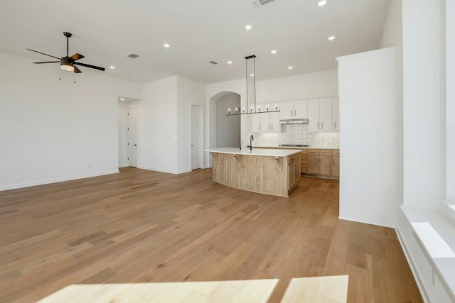 kitchen featuring white cabinetry, a center island with sink, pendant lighting, light hardwood / wood-style floors, and backsplash