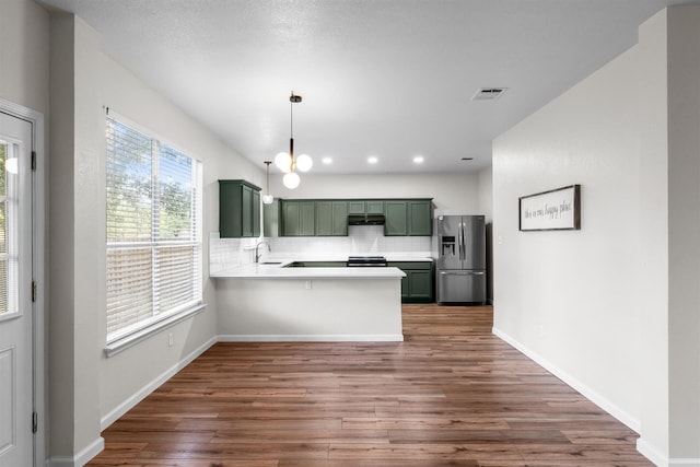 kitchen featuring tasteful backsplash, wood-type flooring, sink, kitchen peninsula, and stainless steel fridge