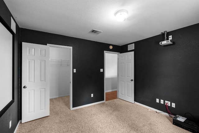 unfurnished bedroom with a spacious closet, a closet, a textured ceiling, and carpet floors