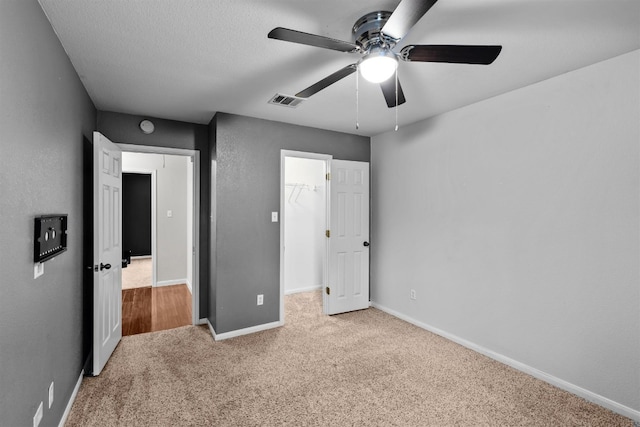 unfurnished bedroom with light colored carpet, ceiling fan, a closet, and a walk in closet