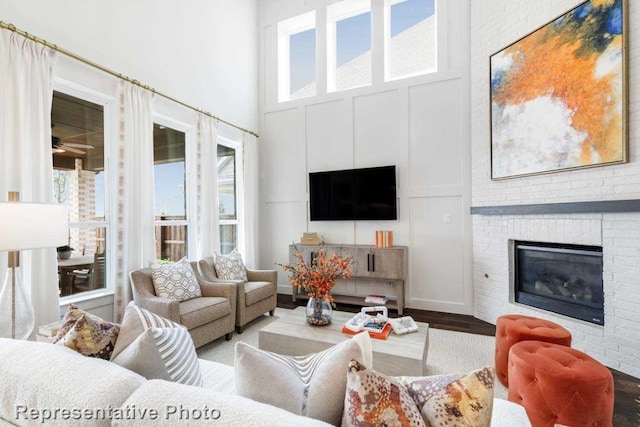 living room featuring a high ceiling, wood-type flooring, a healthy amount of sunlight, and a brick fireplace