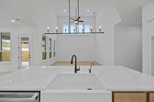 kitchen with a center island with sink, hanging light fixtures, light stone countertops, sink, and dishwasher