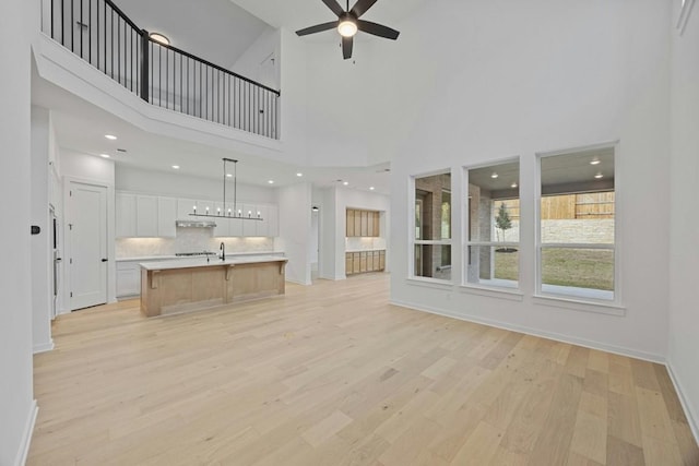 unfurnished living room with light hardwood / wood-style flooring, ceiling fan, and a towering ceiling