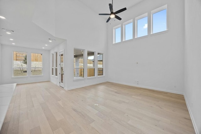 unfurnished living room with ceiling fan, a high ceiling, and light hardwood / wood-style floors