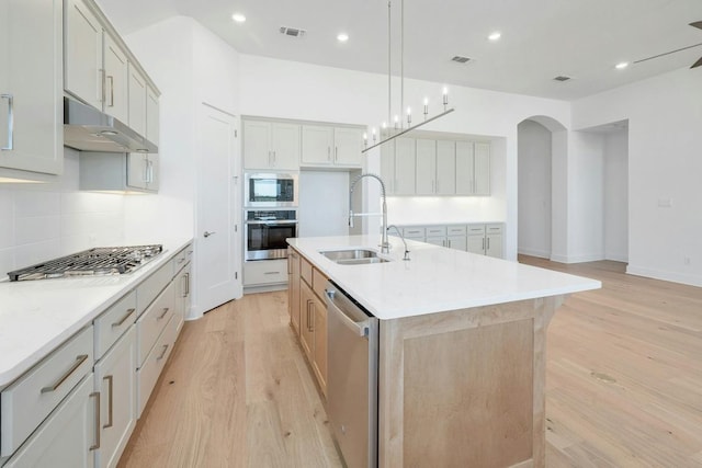 kitchen featuring appliances with stainless steel finishes, a sink, light wood-type flooring, decorative backsplash, and light countertops