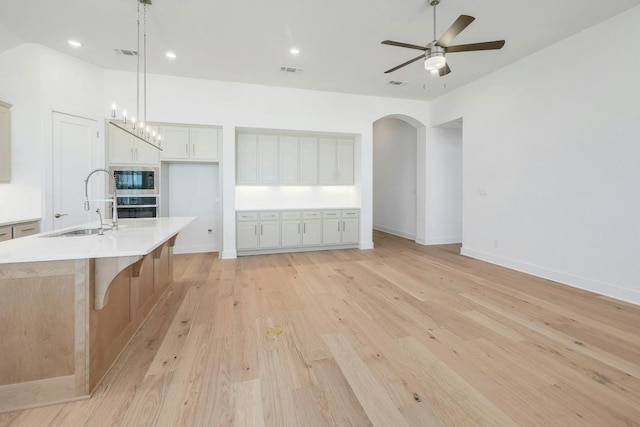 kitchen with a sink, appliances with stainless steel finishes, an island with sink, arched walkways, and light wood finished floors