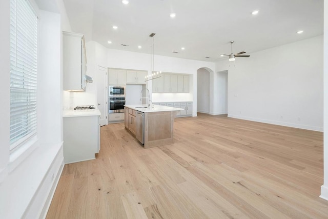 kitchen featuring appliances with stainless steel finishes, ceiling fan, arched walkways, an island with sink, and a sink