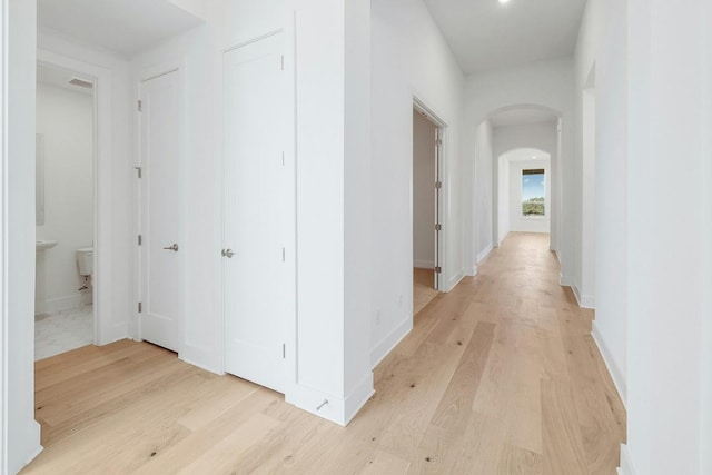 hall with arched walkways, light wood-type flooring, and baseboards