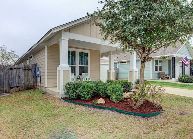 view of front of property featuring a front lawn, fence, covered porch, and board and batten siding