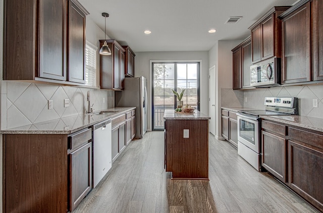 kitchen featuring sink, a center island, light stone counters, light hardwood / wood-style floors, and appliances with stainless steel finishes