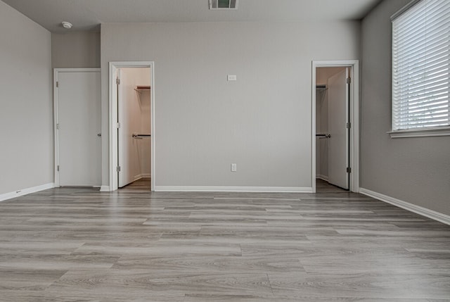 unfurnished bedroom featuring light wood-type flooring, a spacious closet, connected bathroom, and a closet