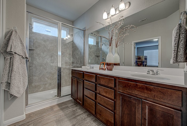 bathroom featuring double vanity, a shower stall, wood finished floors, and a sink